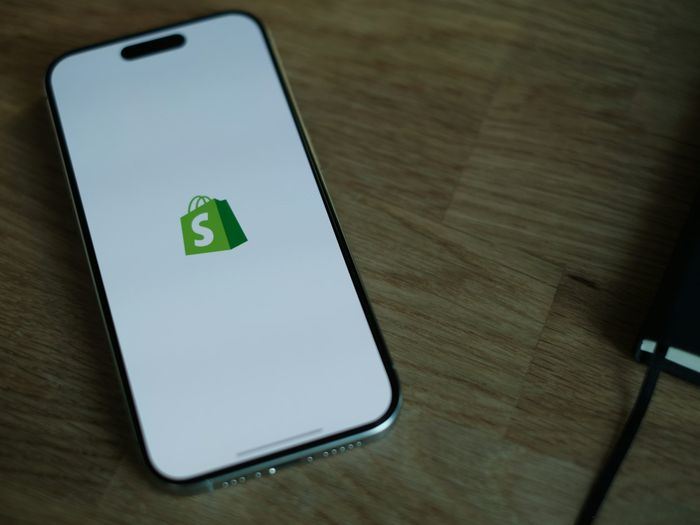 Móvil con el logotipo de Shopify sobre una mesa de madera, imagen de las apps a medida para Shopify